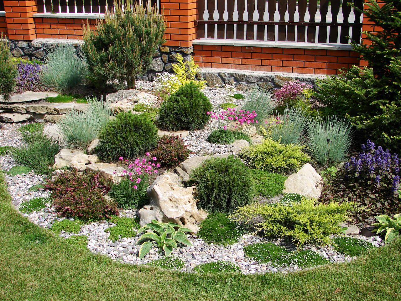 A serene rock garden featuring an array of smooth grey stones arranged in an elegant pattern with green shrubs and flowers.